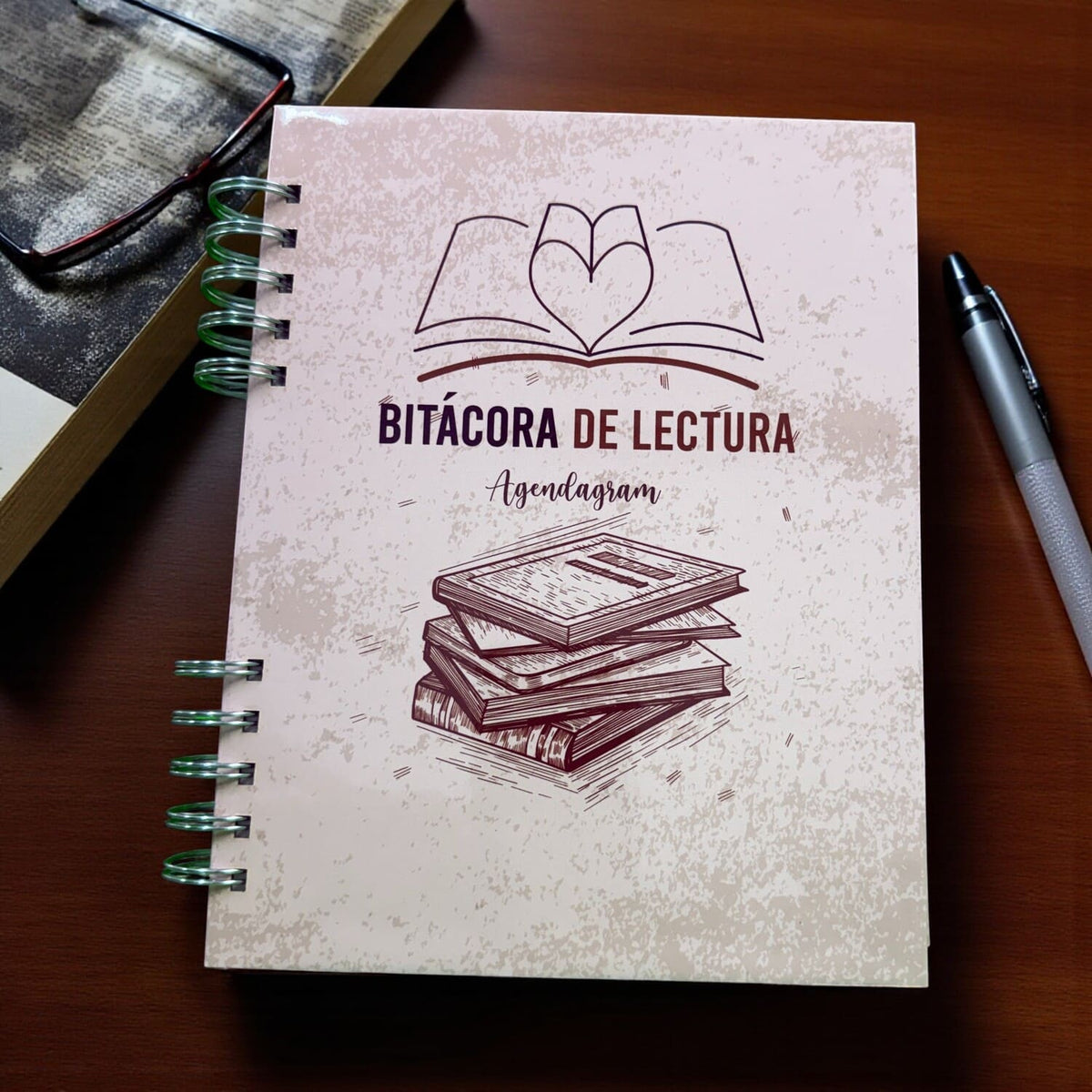 Libro abierto junto a una bitácora de lectura iNMente para escribir lo que se recuerda después de leer